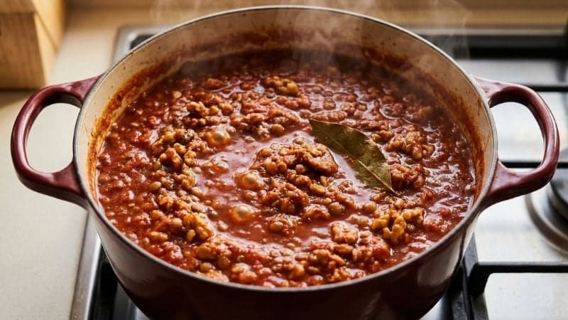 Une casserole remplie de sauce bolognaise vegan épaisse en train de mijoter doucement.