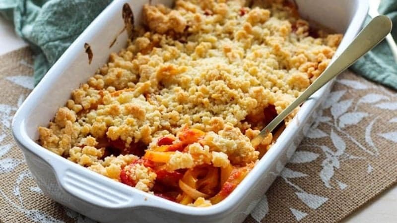 Un crumble salé vegan aux poivrons dans un plat à four blanc avec une belle coloration