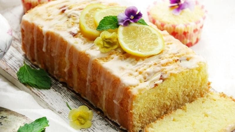 Un magnifique cake au citron vegan découpé avec des fleurs en décoration et des morceaux de citron frais