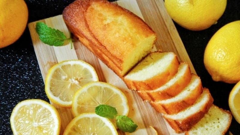 Un très beau cake au citron vegan pour le gouter, posé sur une planche en bois avec des citrons entiers comme décoration