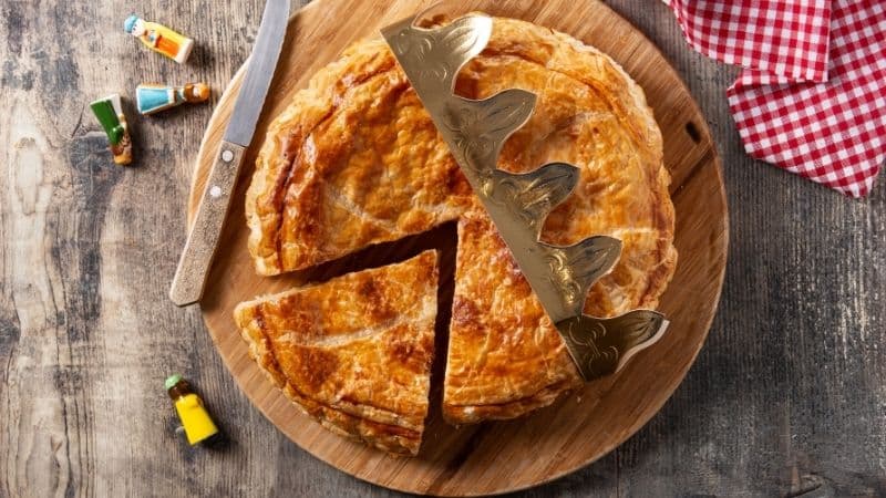 Une galette des rois bien dorée à la frangipane vegan avec une couronne sur un plateau en bois