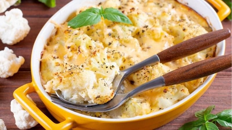 Un gratin de chou-fleur vegan bien crémeux avec des couverts sur le plat