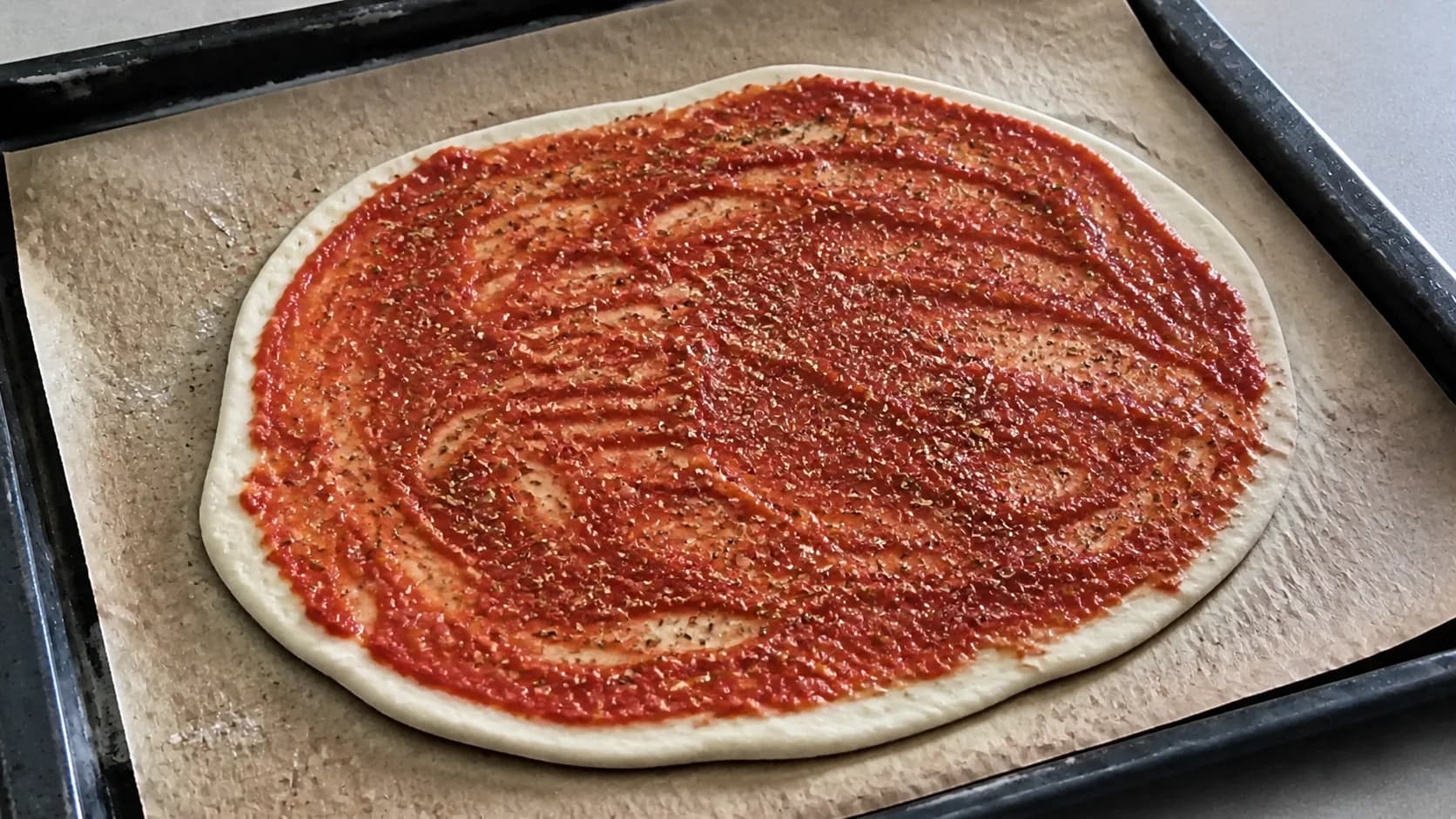 Pâte à pizza étalée recouverte de sauce tomate parsemée d'origan