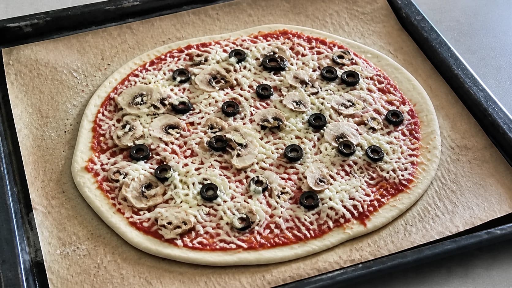 Pizza vegan garnie de mozzarella végétale, champignons et olives avant cuisson