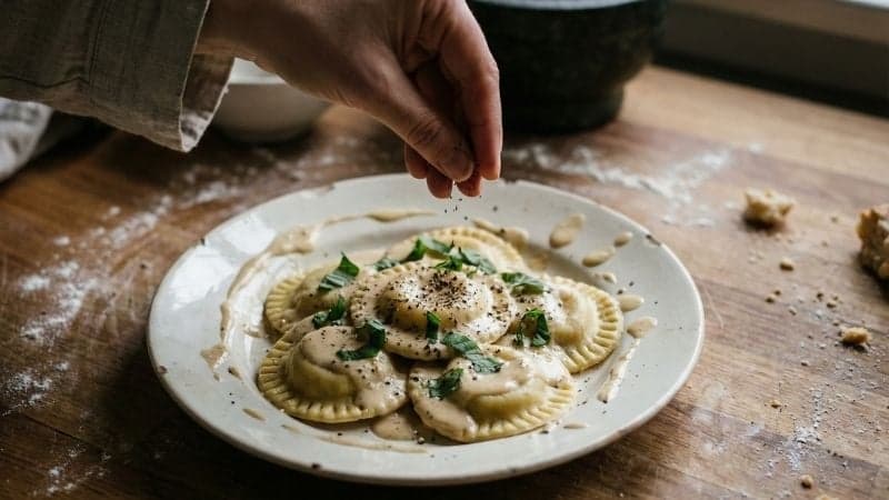 Gros plan sur des raviolis vegan ronds et faits maison, servis avec une sauce onctueuse et du poivre frais.