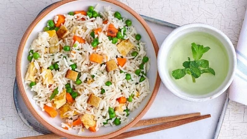 Un riz cantonais vegan avec une petite sauce à la menthse et des baguettes posées sur un plateau