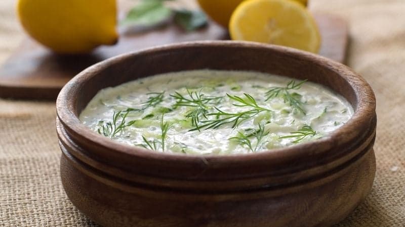 Un Tzatziki Vegan avec quelques feuilles d'aneth en topping et quelques citrons en arrière plan