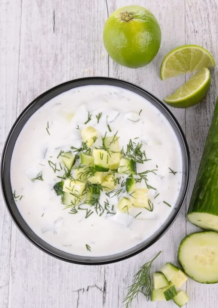 Un Tzatziki Vegan bien crémeux dans un bol noir avec un concombre et un citron en décoration